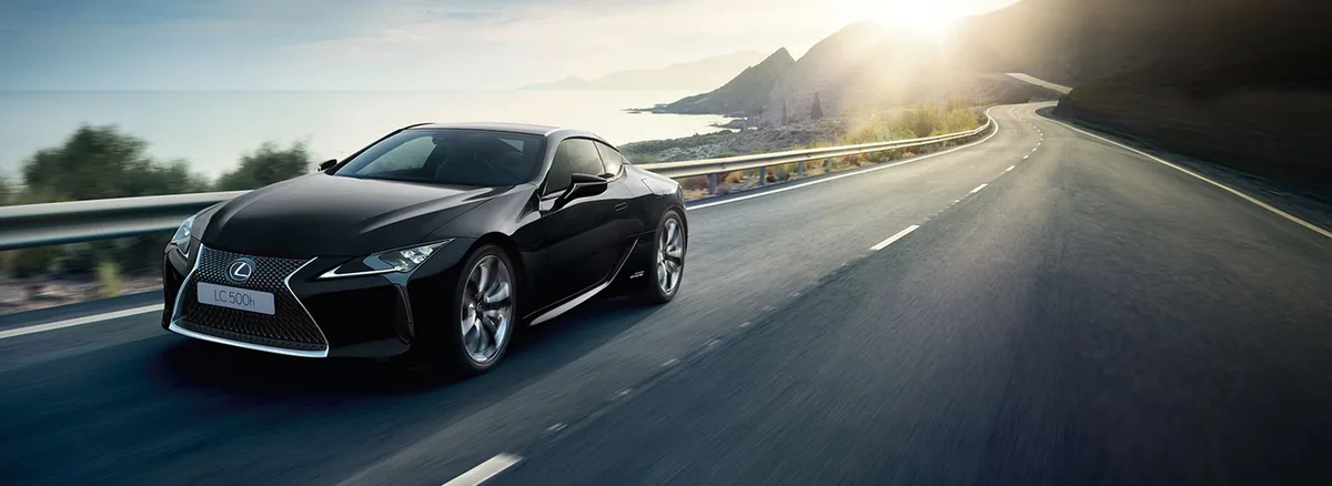 Černý Lexus LC 500h na pobřežní silnici v protisvětle